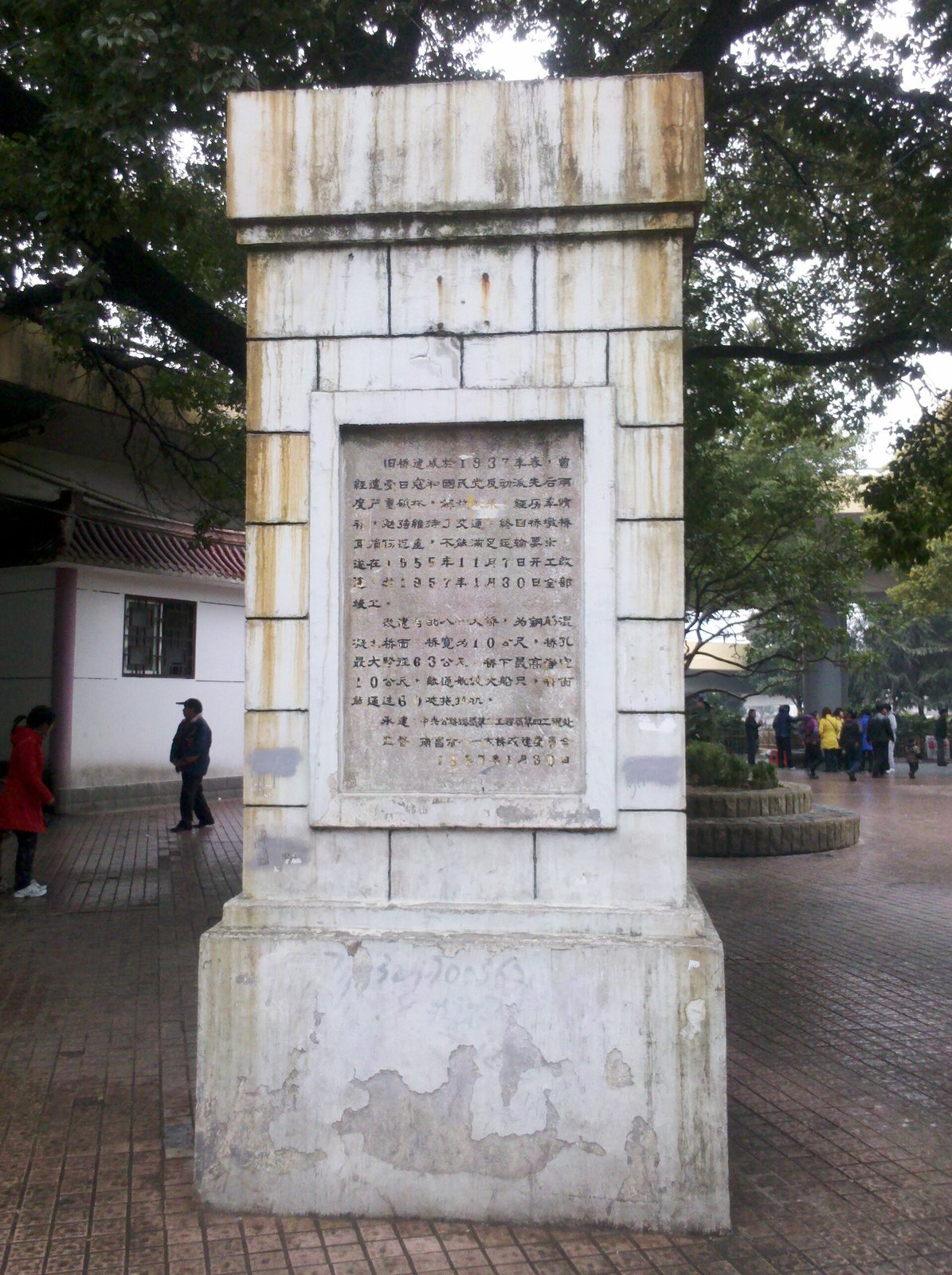 The whitewashed stone pillar left from the old Bayi Bridge in Nanchang, with a carved stone tablet dated 30 January 1957 set into its face, standing on a paved square under the bridge approach