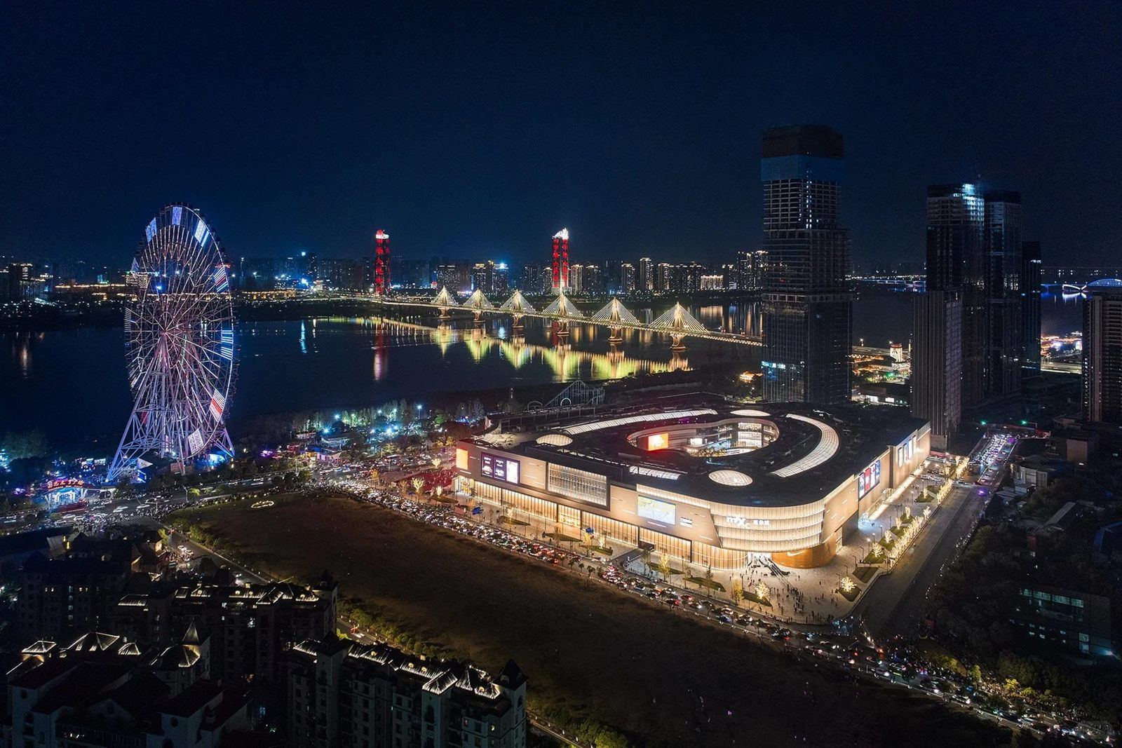 Night aerial of the Star of Nanchang Ferris wheel lit up beside the Gan River, with the illuminated Bayi Bridge and city skyline