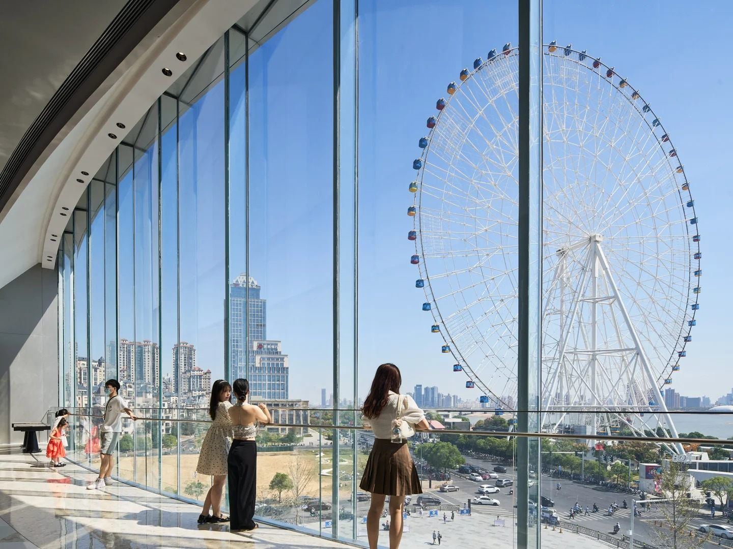 Visitors at the floor-to-ceiling windows inside Nanchang MixC looking out at the Star of Nanchang Ferris wheel and the Gan River