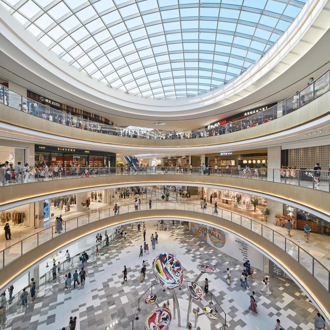 The oval atrium of Nanchang MixC, with curved balconies, a glass skylight and a sculpture on the ground floor