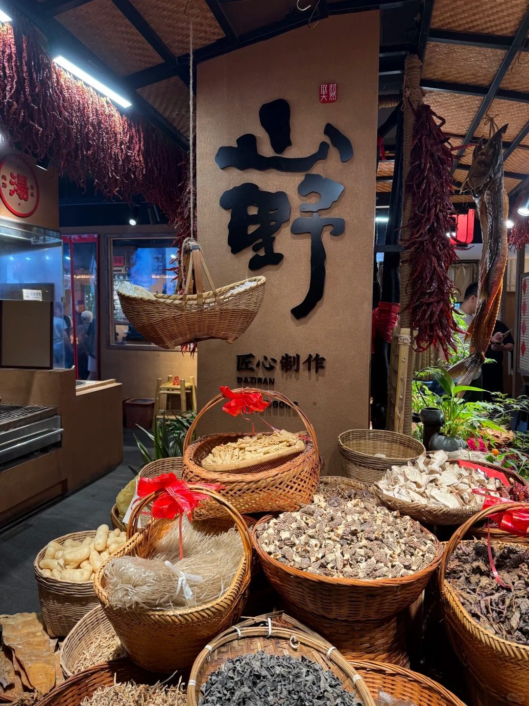 Strings of dried red chillies hanging above baskets of dried mushrooms and vermicelli at a Jiangxi restaurant, with a dried fish hung alongside.