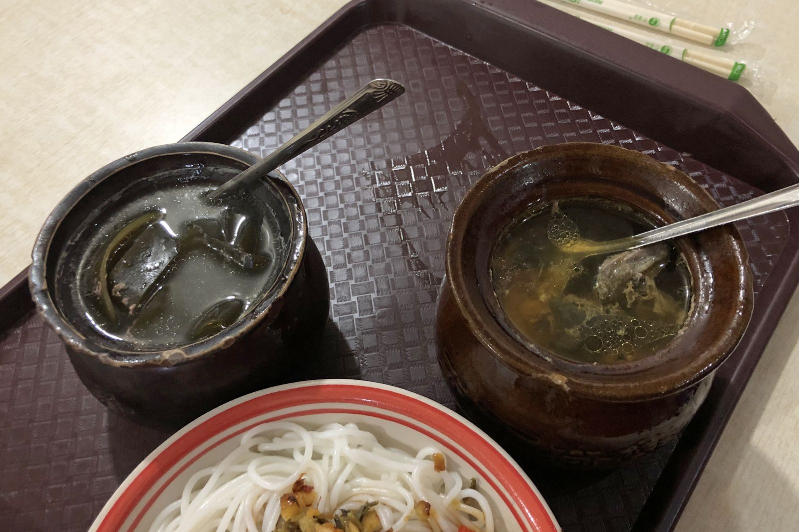 Two earthenware crock pots of Nanchang waguantang soup on a tray beside a bowl of rice noodles