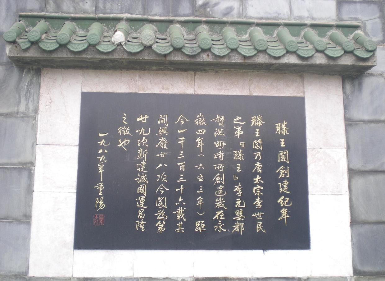 A black stone tablet set in a grey brick wall under a green-tiled coping, its gold-inlaid running-script inscription headed 滕王阁创建纪年 and signed 一九八九年重阳 with a red seal.