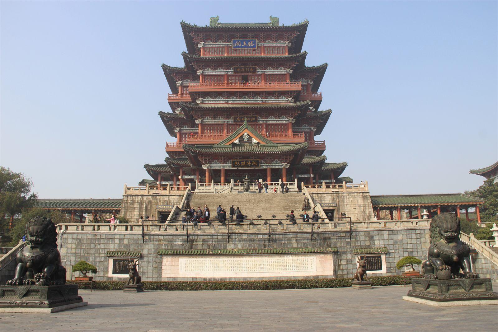 Tengwang Pavilion in Nanchang seen head-on from the entrance plaza: tiers of jade-green glazed eaves and vermilion pillars above a stone terrace, with bronze lions flanking the steps and visitors on the stairs.