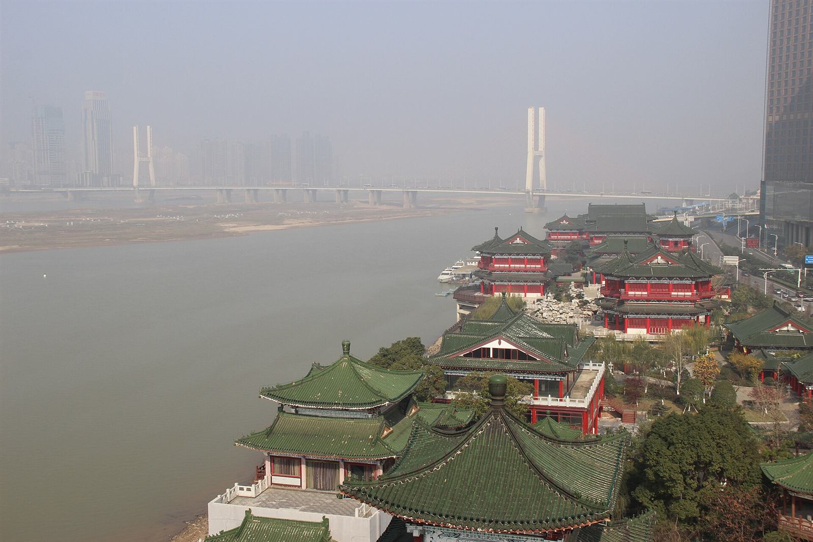 The view from the top of Tengwang Pavilion: green pavilion roofs in the foreground, the wide Gan River, the Bayi cable-stayed bridge, and the Honggutan high-rise skyline on the far bank.