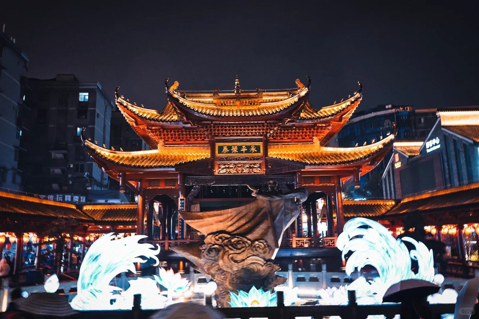 A night light-show at Wanshou Palace: a great bronze flood-dragon sculpture on the pavilion stage rising above blue projected waves and glowing lotus lights